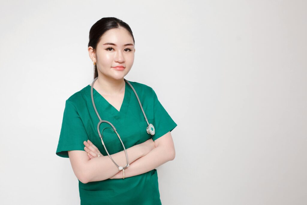 Portrait of a confident nurse in green scrubs with crossed arms and stethoscope, indoor studio setting.