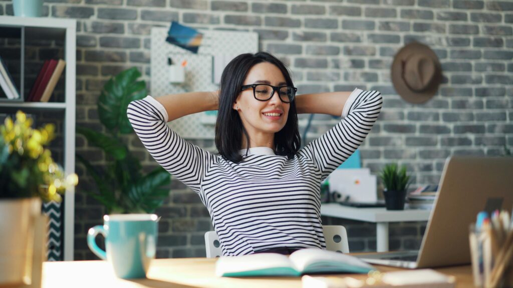 Smiling woman in striped blouse relaxing at desk in a modern home office environment.