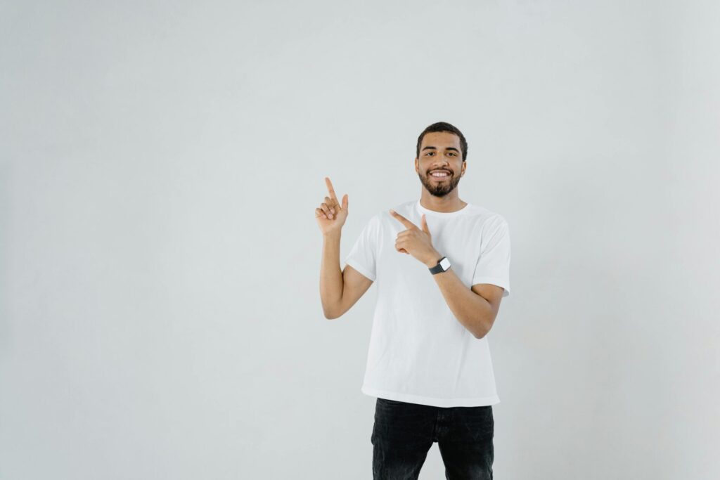African American man in white shirt smiling and pointing against blank background.