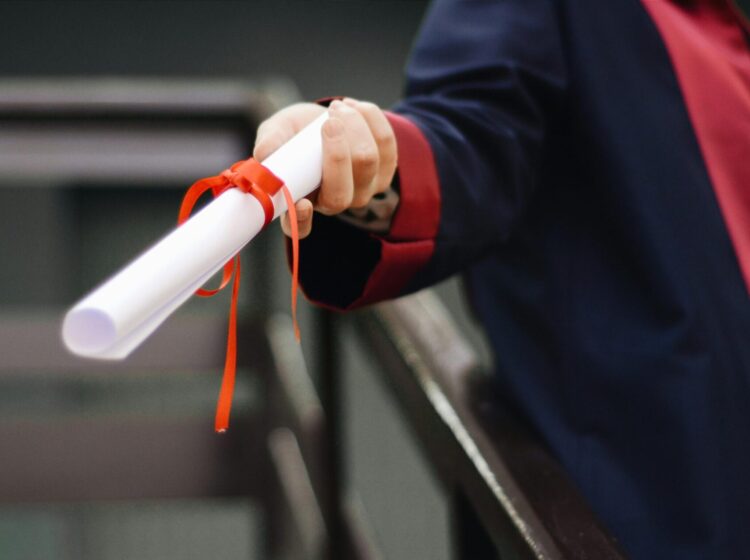 A close-up image of a graduate holding a diploma tied with a red ribbon, symbolizing achievement and success.