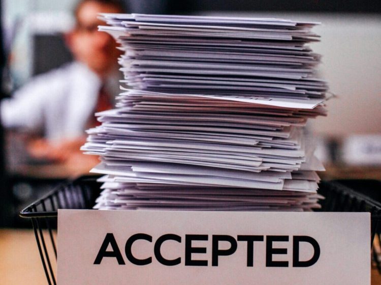 Pile of papers with 'Accepted' label in a busy office setting, highlighting information management.