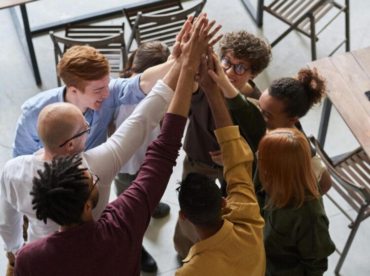 A diverse group of professionals high-fiving in a modern office, showcasing teamwork and collaboration.