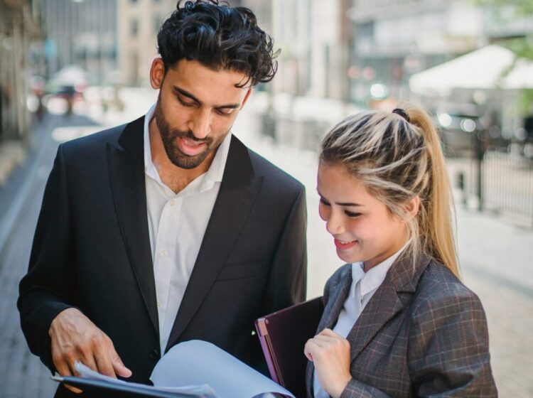 Young business professionals in formal attire reviewing documents outdoors, showcasing teamwork.